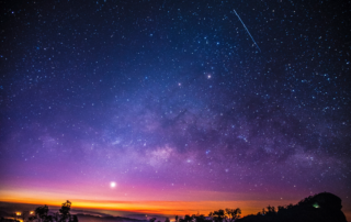 A photograph of a cold, clear, starry night. The colours range from orange close to the horizon upwards to deep purple (almost black).